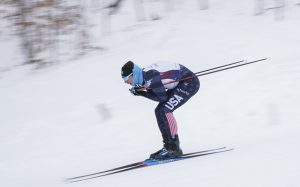 A cross-country skier at the 2023 FISU games, representing USA, is skiing downhill.