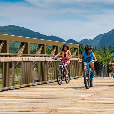 A mother and her two daughters, along with their biking guide are biking across a bridge with the Adirondack Mountains as their backdrop.