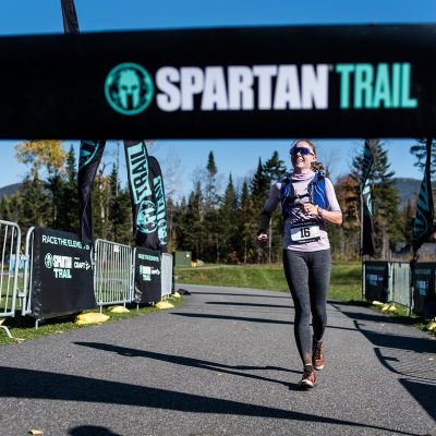 A female runner crosses the finish line at a Spartan Trail Race at Mt Van Hoevenberg.