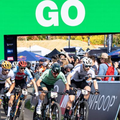 A mass start of riders at Mt Van Hoevenberg with a big green sign behind them that says, "GO."
