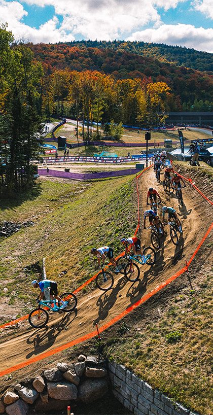 Fall drone shot from the UCI Mtb World Series event showing racers biking down a berm hill.